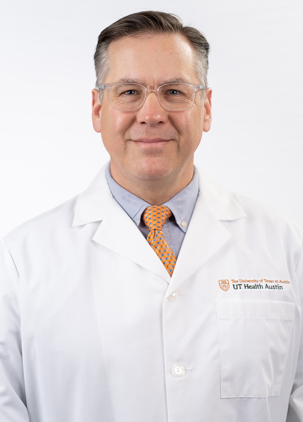 Perfusionist William "Richard" Owens, BS-MT, CCP, FPP, LP smiling in front of a white backdrop. He is wearing a white coat with an embroidered UT Health Austin logo.