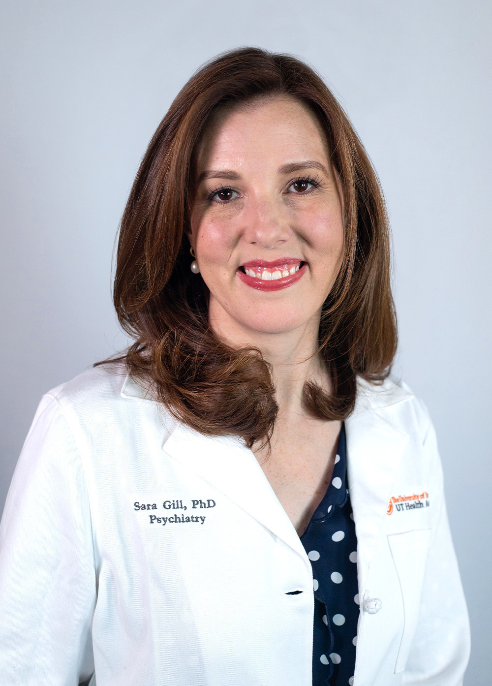 Pediatric psychologist Sara Gill, PhD, wearing a white coat and smiling in front of a white backdrop.