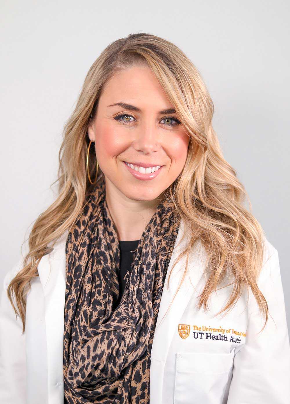 Sarah Felderhoff wearing a white coat and leopard print scarf and smiling in front of a white backdrop.