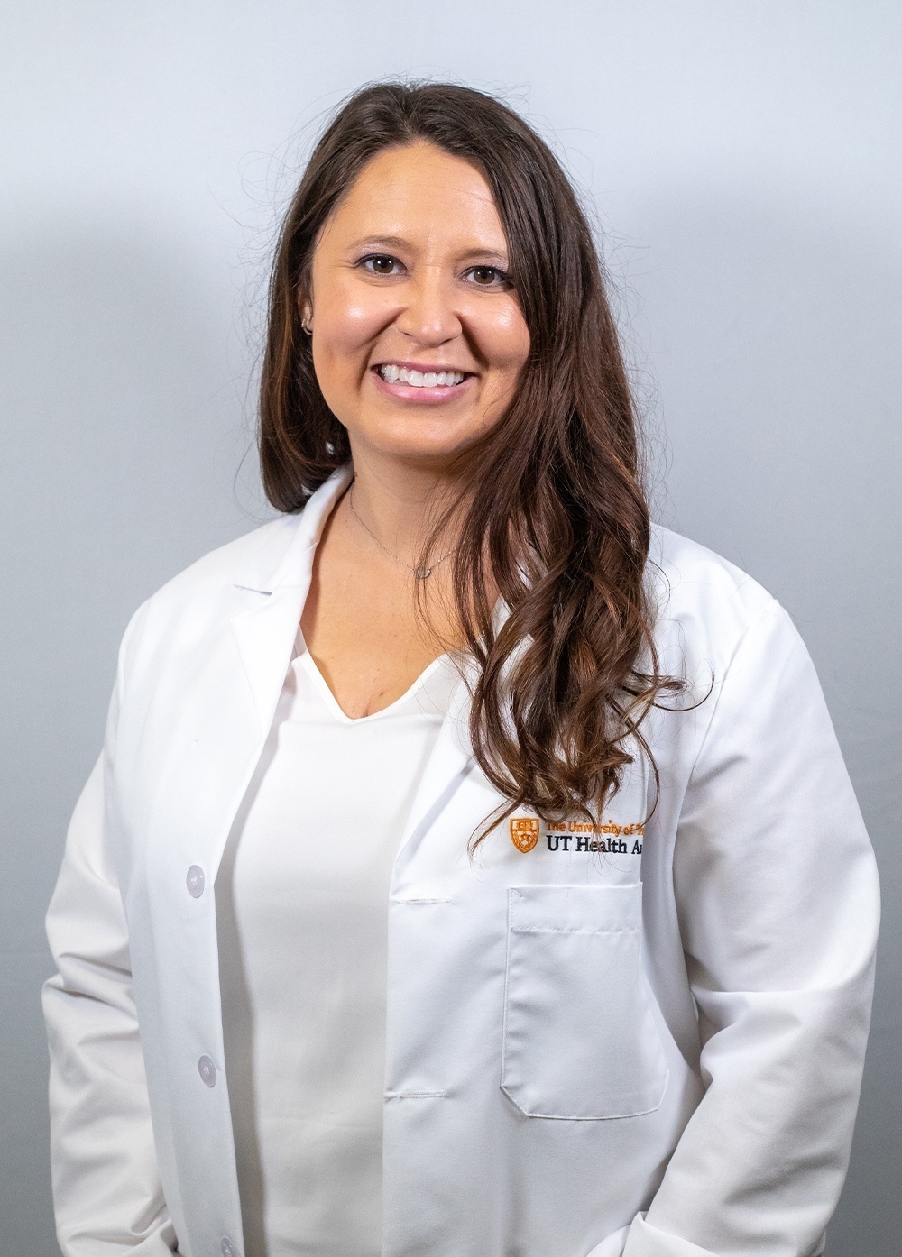 Pediatric psychologist Sasha Jaquez, PhD, wearing a white coat and smiling in front of a white backdrop.