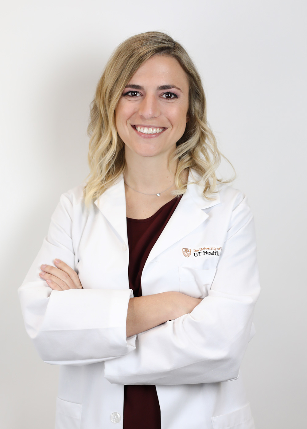 Stephanie Doggett wearing a white coat and smiling in front of a white backdrop.