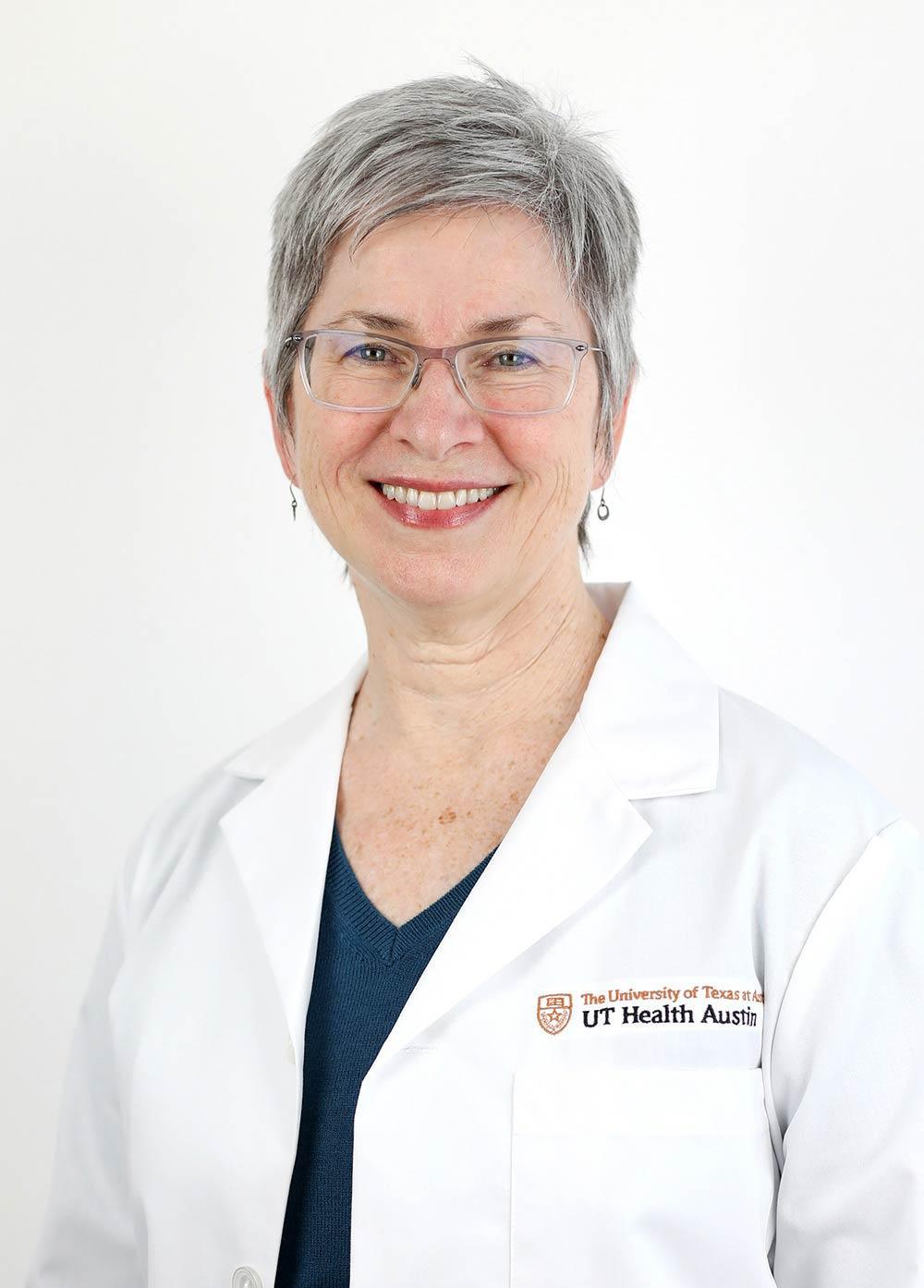 Sylvia Deily wearing a white coat and smiling in front of a white backdrop.