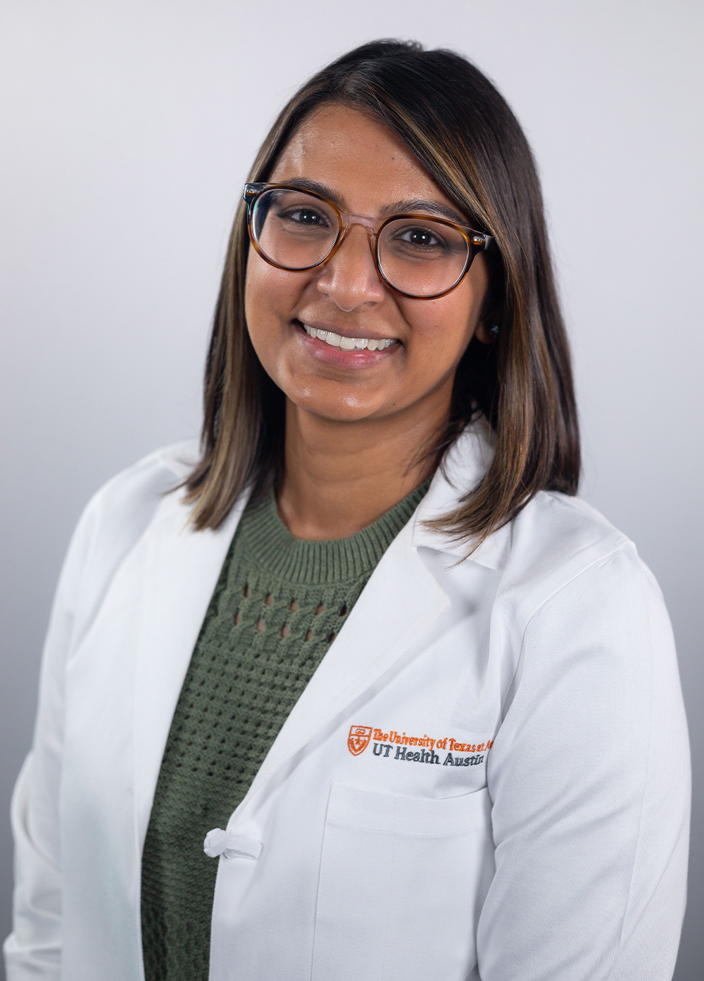 Dr. Veena Patel wearing a white coat and smiling in front of a white backdrop.