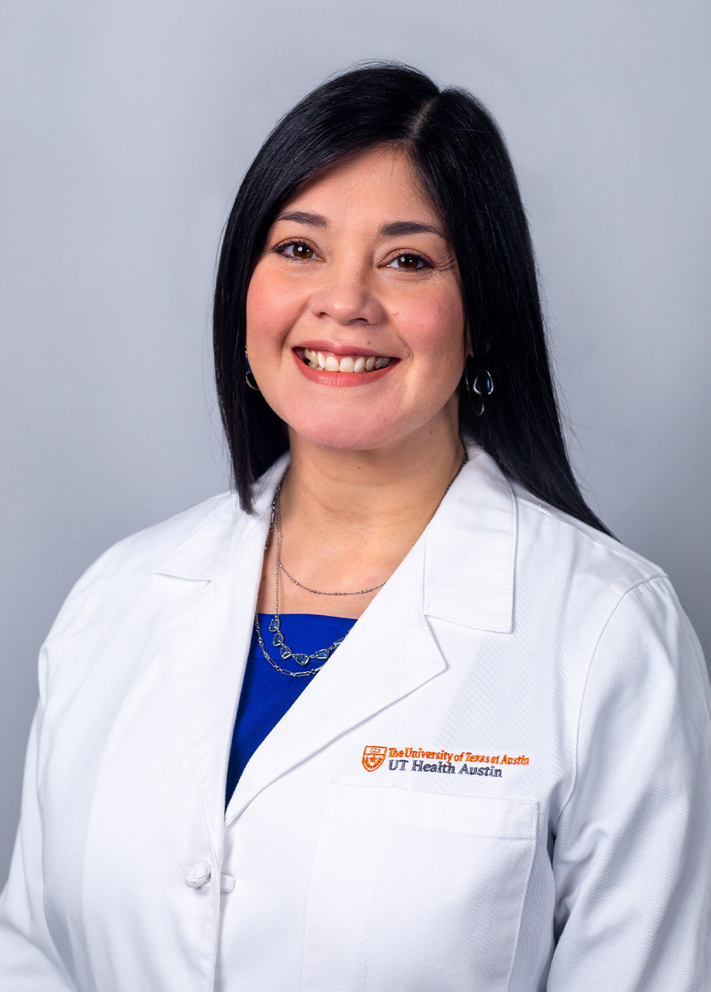 Pediatric nurse practitioner Ligiola Aranaga Sanchez, MSN, APRN, CPNP-PC, wearing a white coat and smiling in front of a white backdrop.