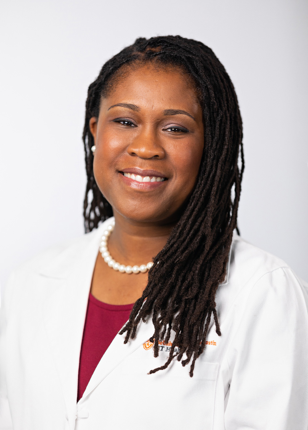 Pediatric and adolescent gynecologist Akua Afriyie-Gray, MD, FACOG, wearing a white coat and smiling in front of a white backdrop.