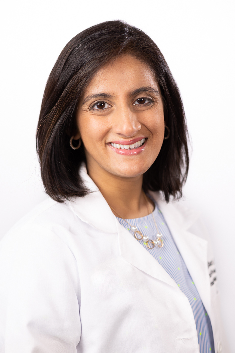 Dr. Alefiyah Malbari wearing a white coat and smiling in front of a white backdrop.