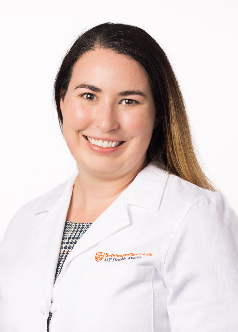 Pelvic floor physical therapist Alexandra Guevara, PT, DPT, smiling in front of a white backdrop. She is wearing a white coat with an embroidered UT Health Austin logo.