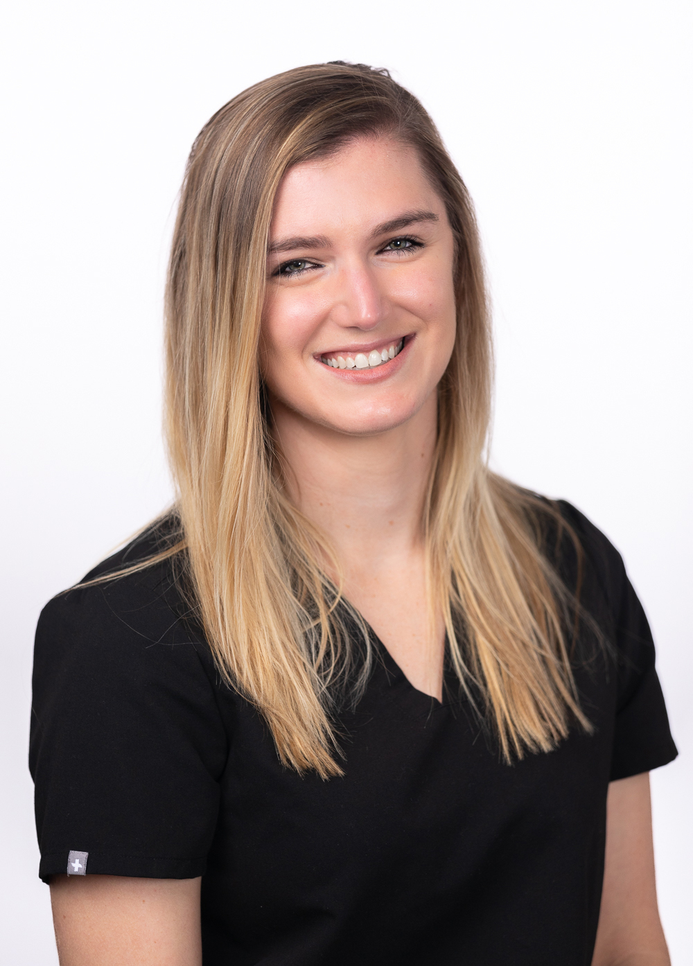 Ann Phillips wearing black scrubs and smiling in front of a white backdrop.