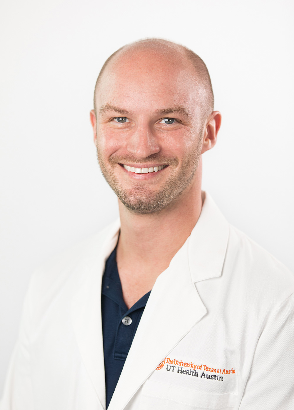 Branden Daubel wearing a white coat and smiling in front of a white backdrop.