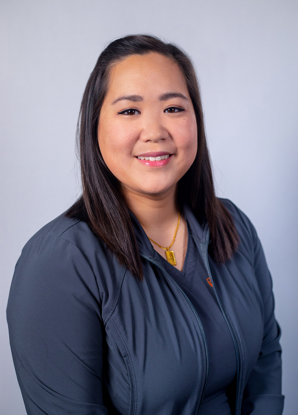 Brittanie Yuen wearing a blue shirt and smiling in front of a white backdrop.