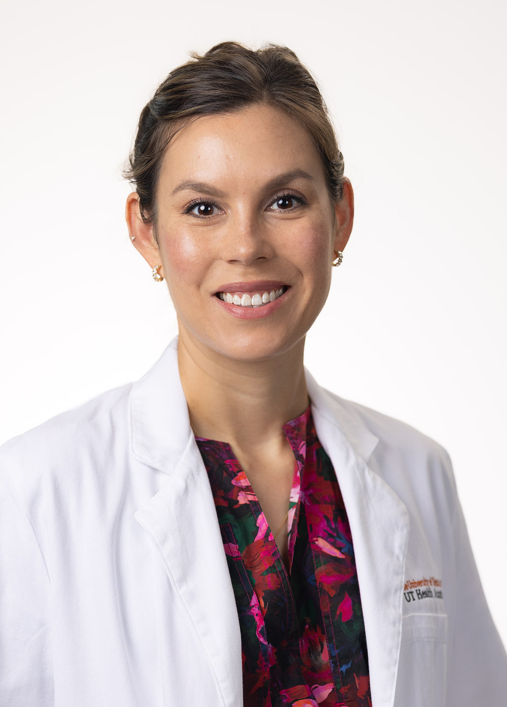 Brittany Rosales, MD, is wearing a white coat and a black and pink floral blouse and is smiling at the camera.