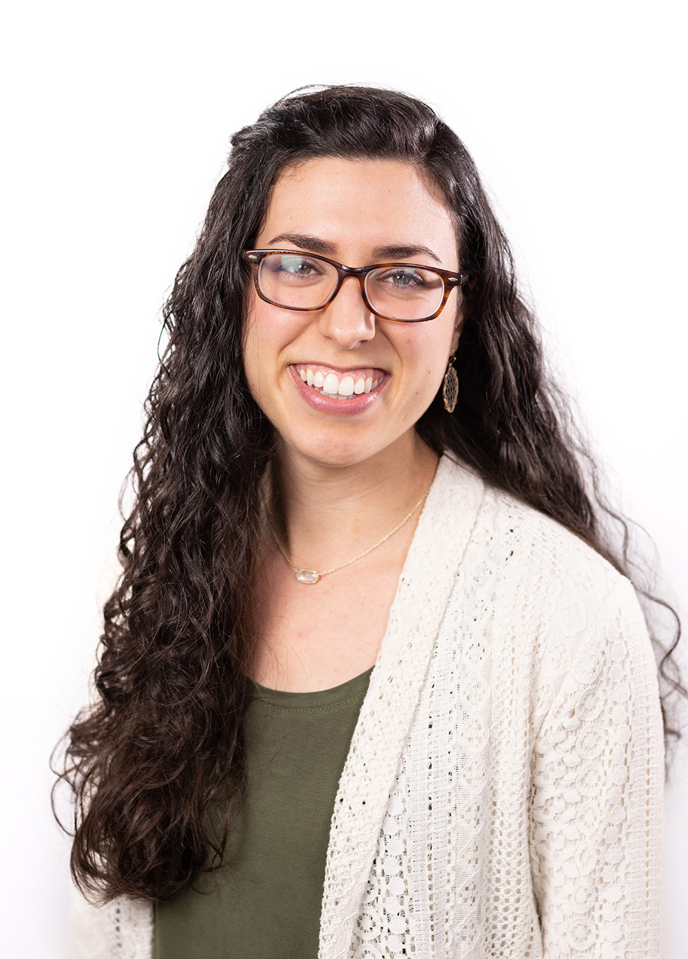 Carla Cos wearing a green shirt and light colored cardigan and smiling in front of a white backdrop.