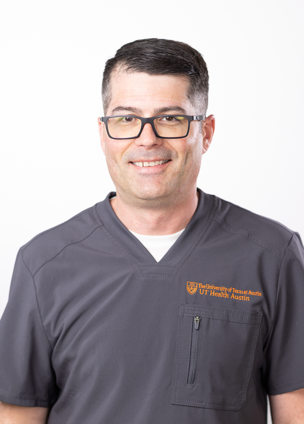 Christopher Mullins wearing dark scrubs and smiling in front of a white backdrop.