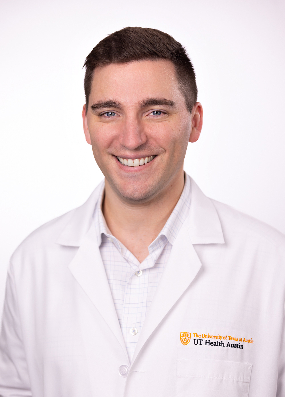 Dr. Christopher Mardy wearing a white coat and smiling in front of a white backdrop.