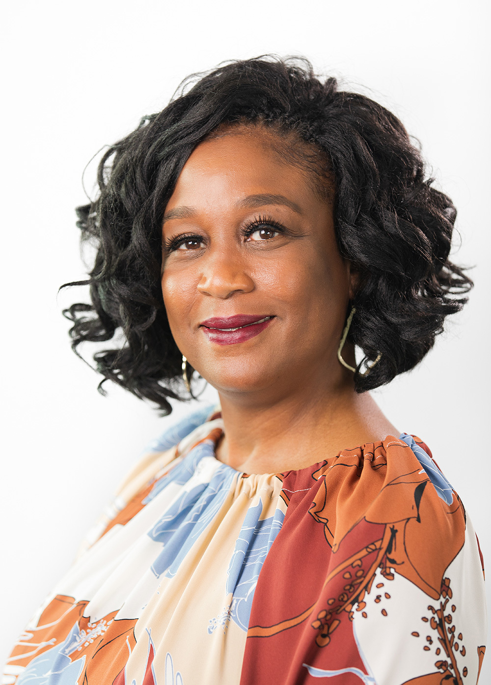 Cicely Cyphers wearing a blue and orange blouse and smiling in front of a white backdrop.