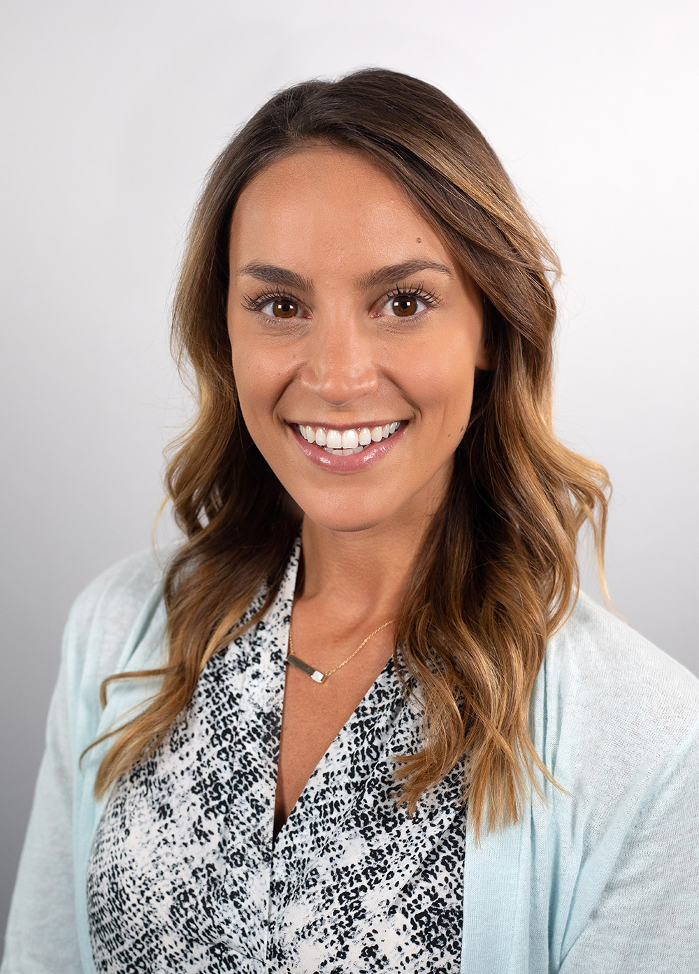 Nutritionist Clara Di Vincenzo wearing a blue cardigan and patterned blouse and smiling in front of a white backdrop.