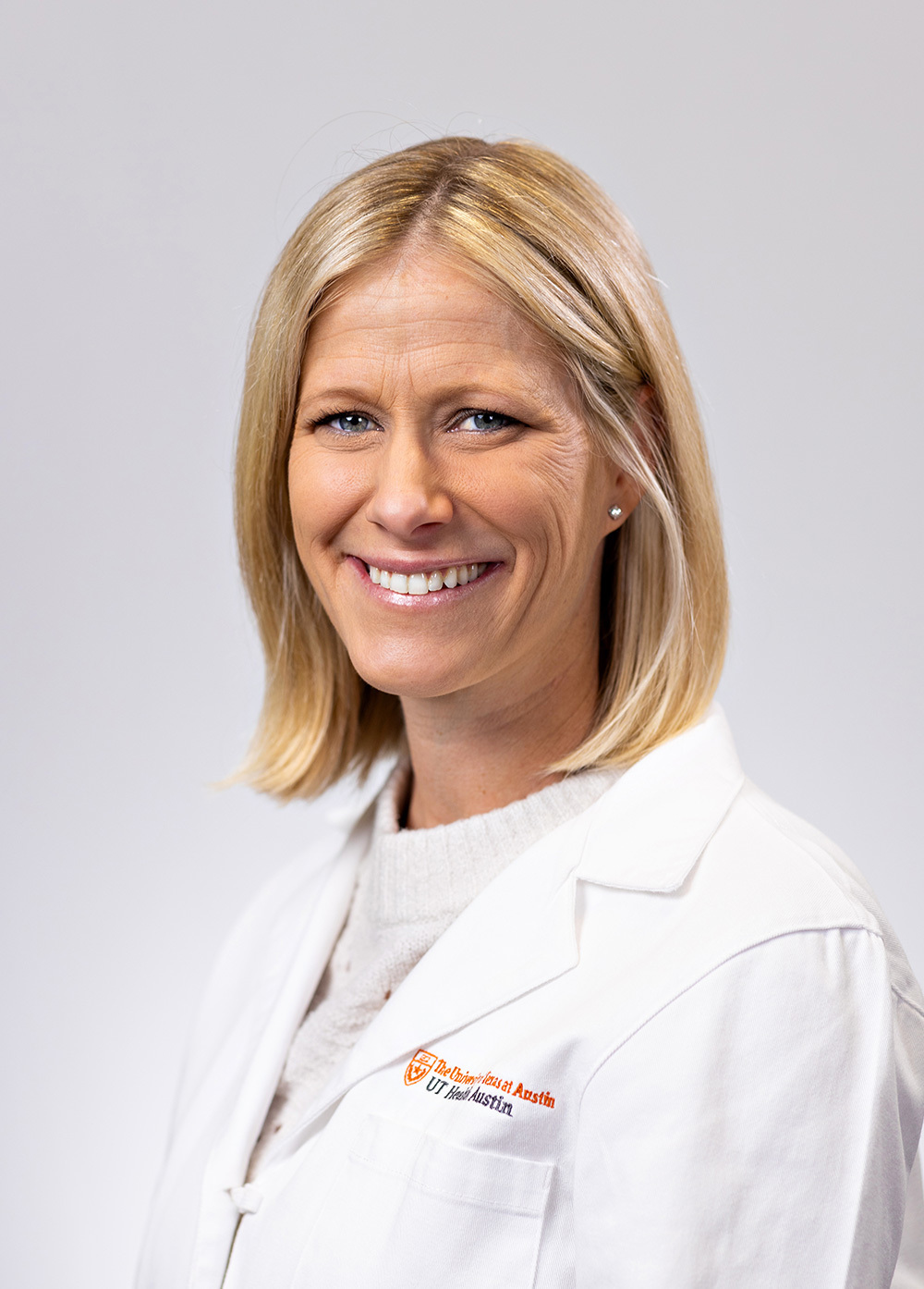 Acute care pediatric nurse practitioner Elizabeth McBrearty, APRN, CPNP-AC, wearing a white coat and smiling in front of a white backdrop.