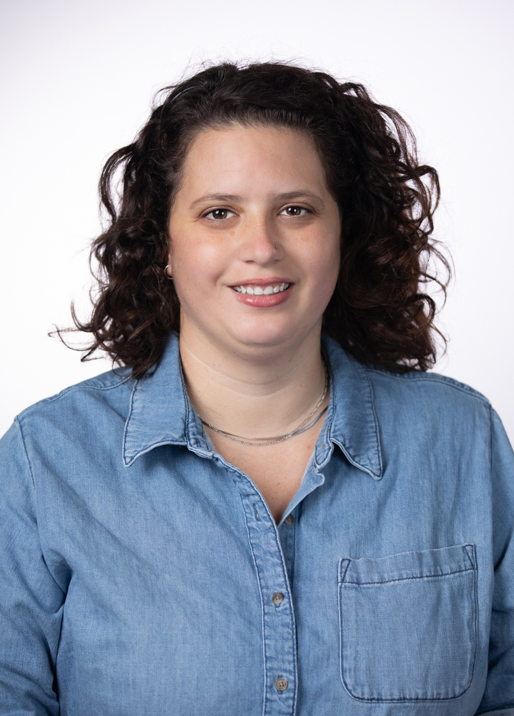 Social worker Emily Brooke, LCSW, smiling in front of a white backdrop. She is wearing a chambray shirt and silver necklaces.