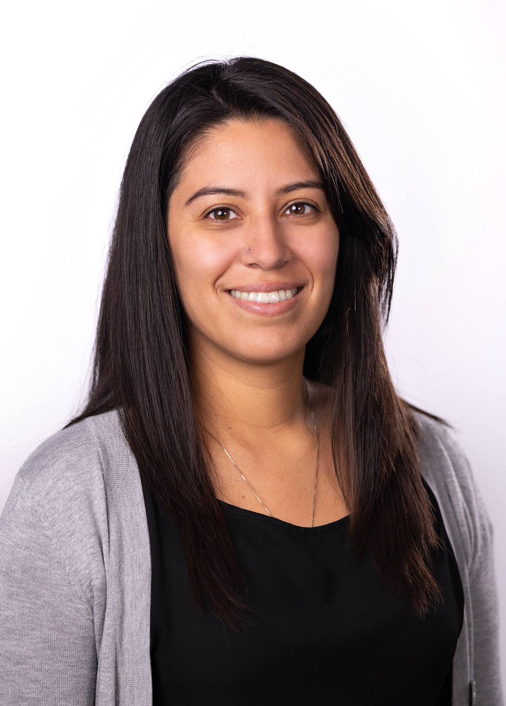 Erika Aurioles wearing a black shirt and gray cardigan and smiling in front of a white backdrop.