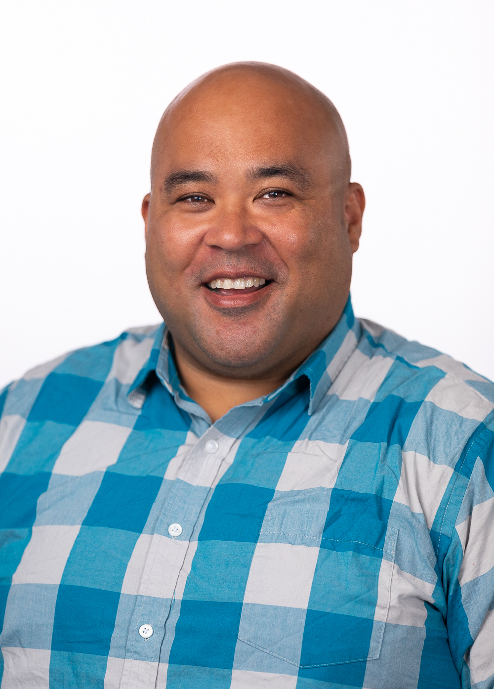 Geoffrey Vasile wearing a checkered shirt and smiling in front of a white backdrop.