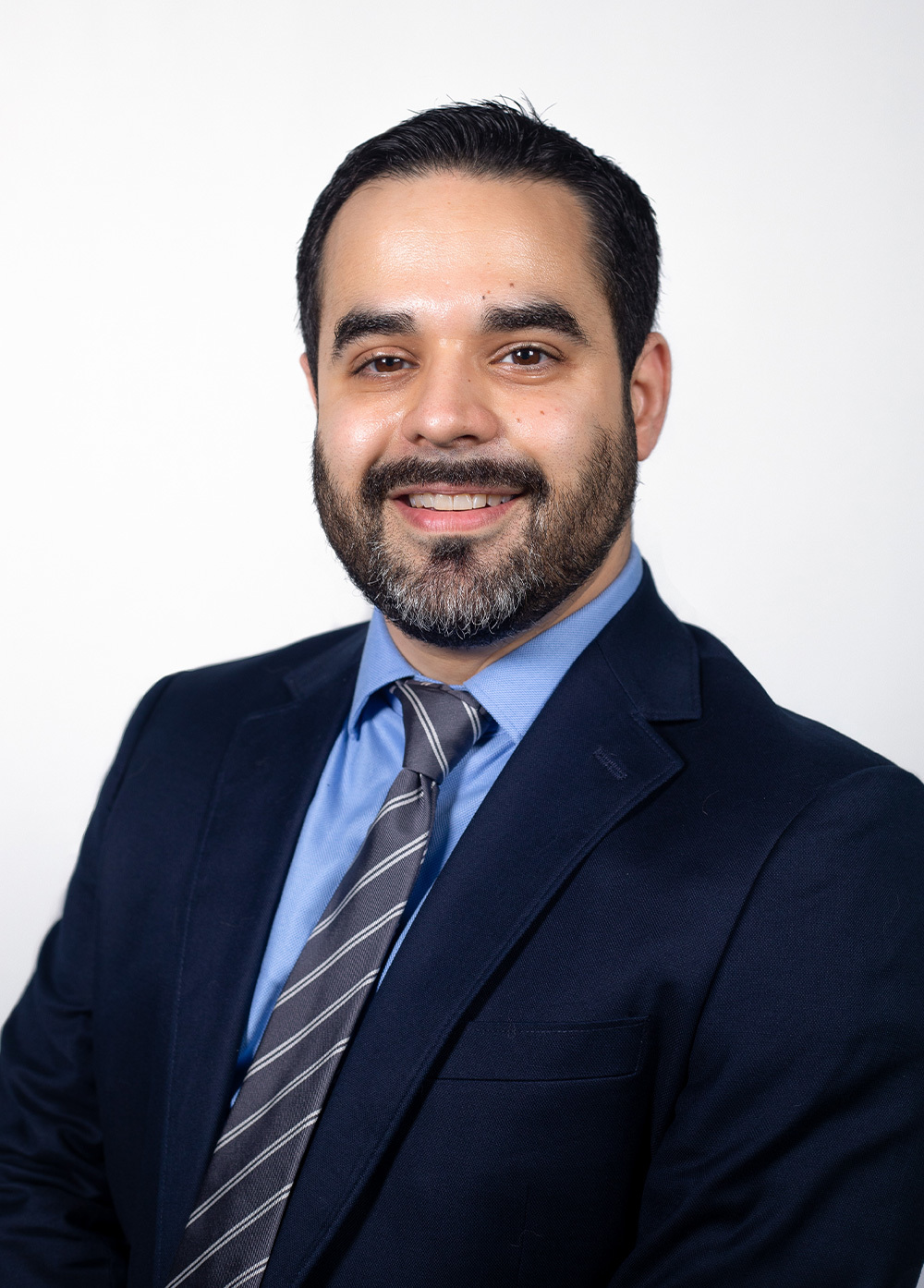 Dr. Greg Fonzo wearing blue suit and striped tie and smiling in front of a white backdrop.