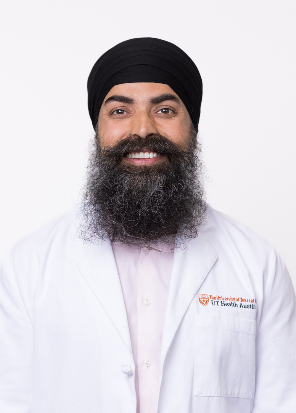 Board-certified orthopedic surgeon Gurpreet Sing, MD, is smiling in front of a white backdrop. He is wearing a white coat with an embroidered UT Health Austin logo.