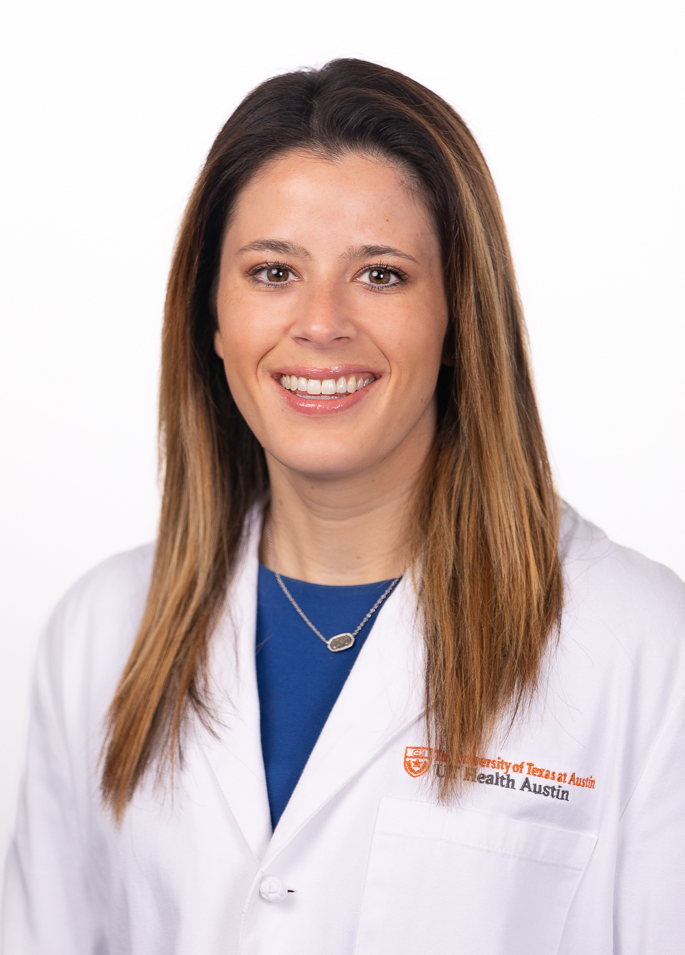 Physician assistant Hannah Coleman, MPAM, PA-C, smiling in front of a white backdrop. She is wearing a white coat with an embroidered UT Health Austin logo.