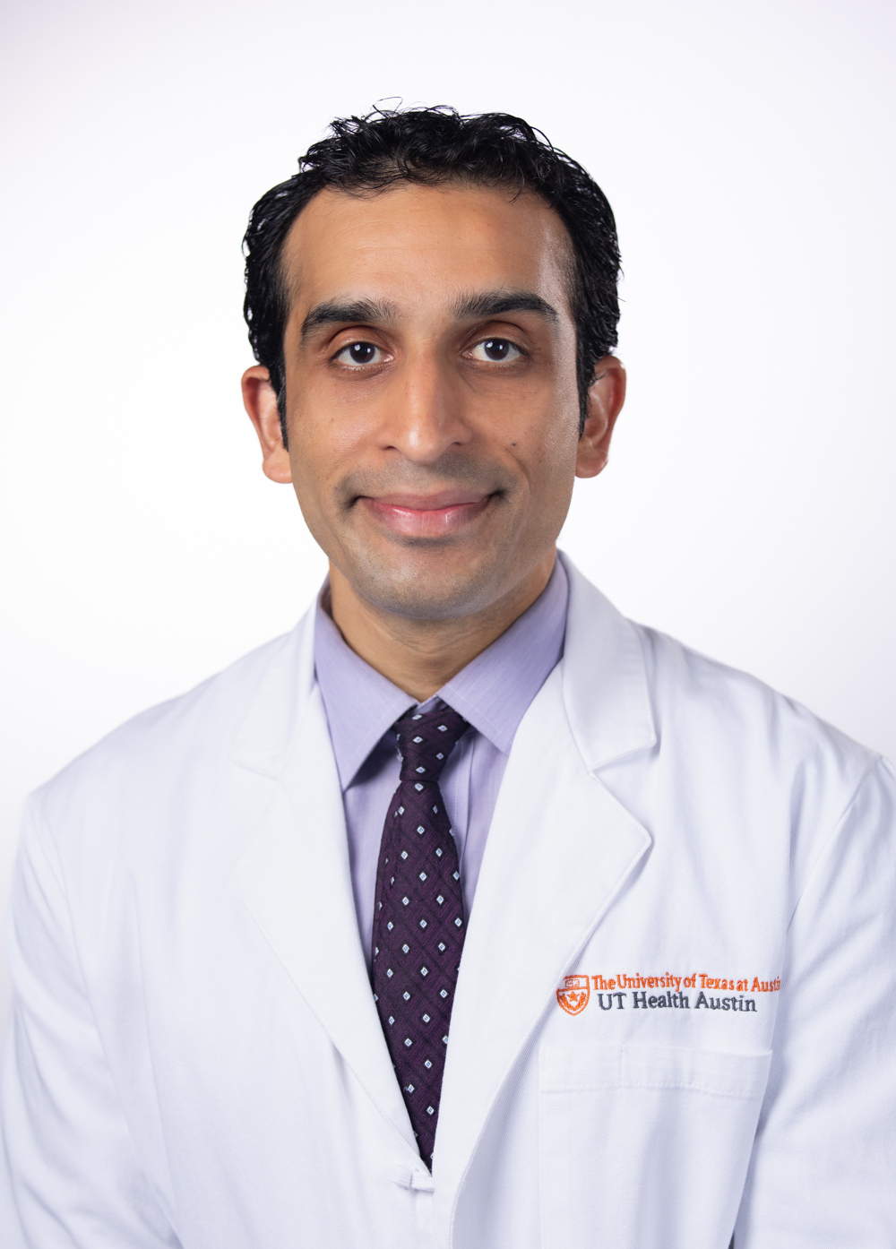 Urologic oncologist Harras Zaid, MD, smiling in front of a white backdrop. He is wearing a white coat with an embroidered UT Health Austin logo.