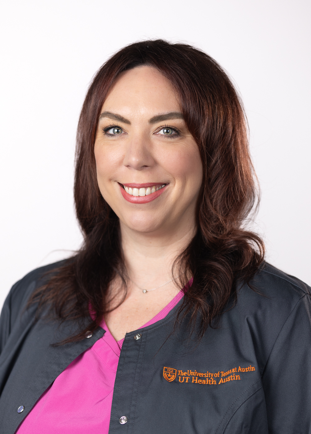 Radiology technologist Jaime Evans wearing a dark jacket embroidered with the UT Health Austin logo and smiling in front of a white backdrop.