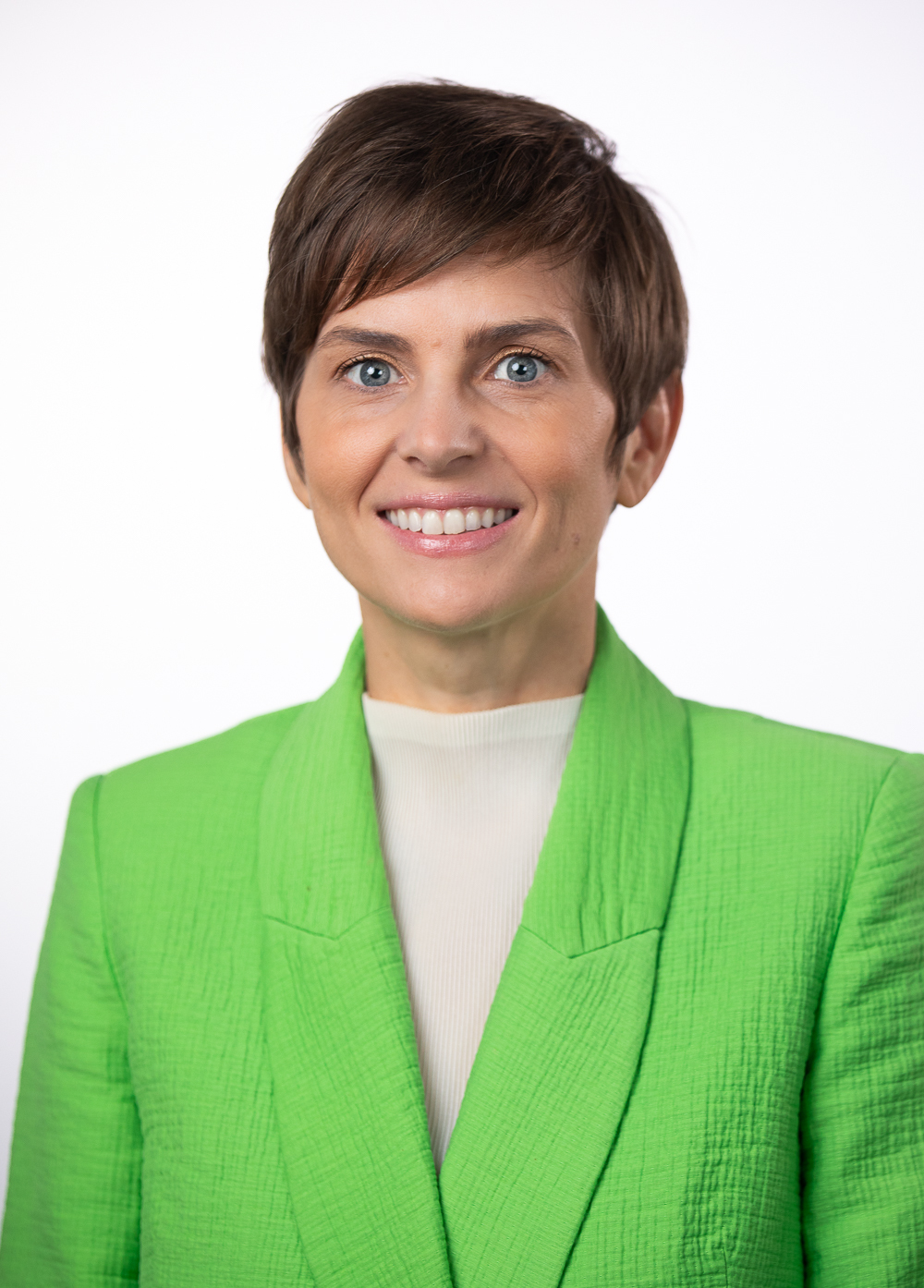 Social worker Jeni Wade, LCSW, smiling front of a white backdrop. She has short brown hair and is wearing a bright green blazer.