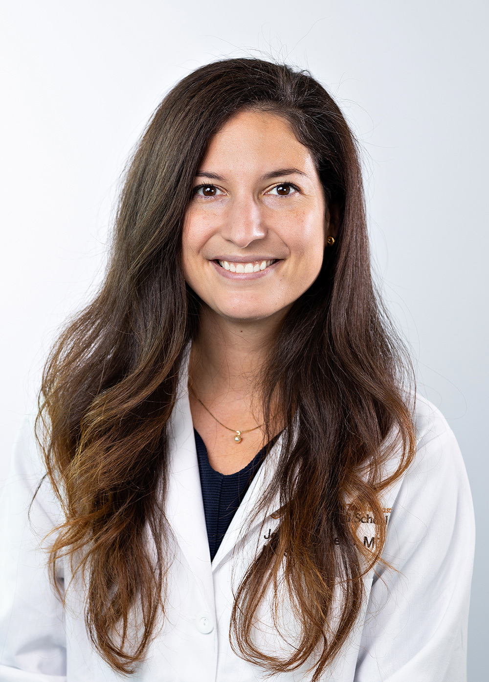 Minimally invasive gynecologic surgeon Jenny Travieso, MD, FACS, wearing a white coat and smiling in front of a white background.