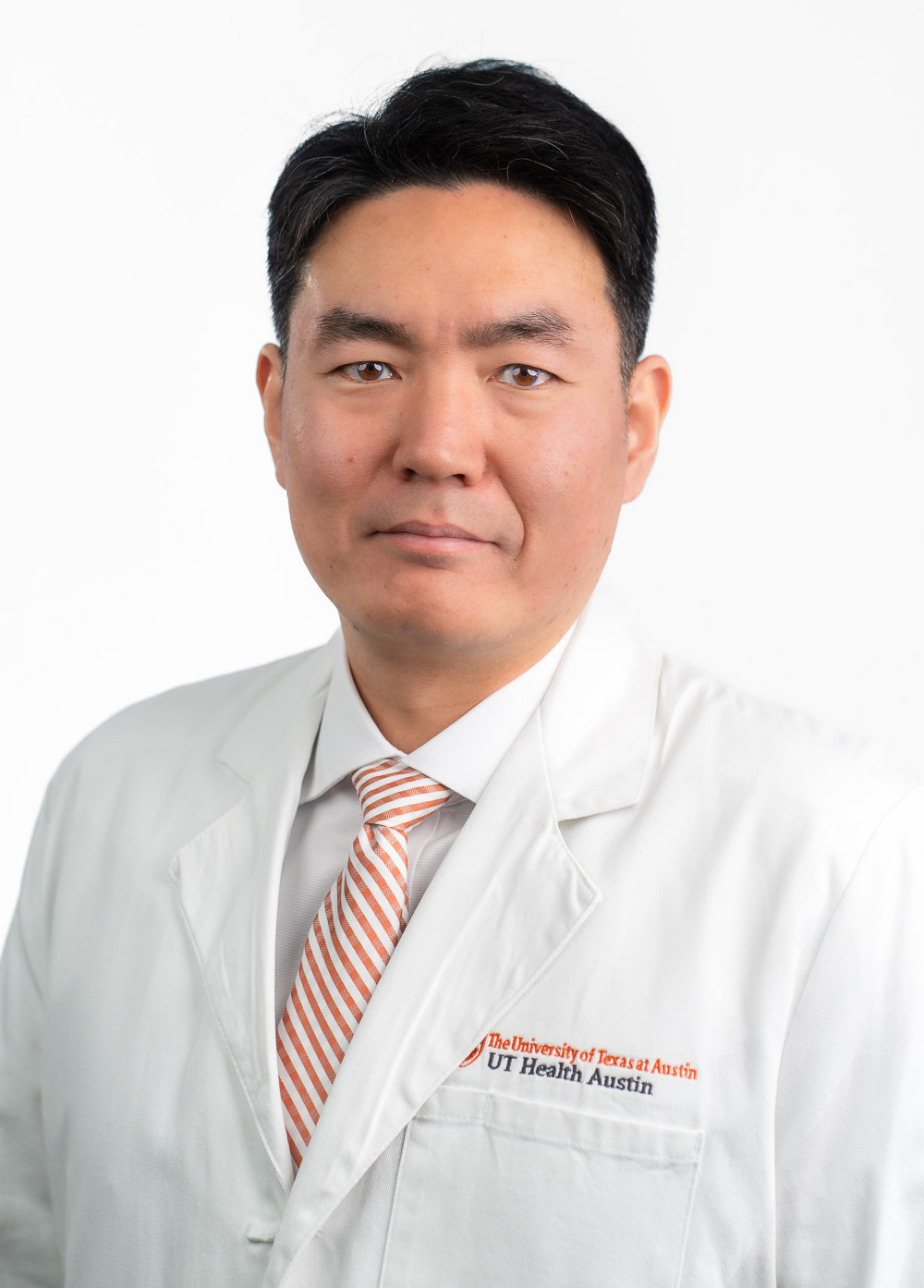 Jiyong Moon is looking at the camera and wearing a white coat with a white shirt and an orange and white striped tie.