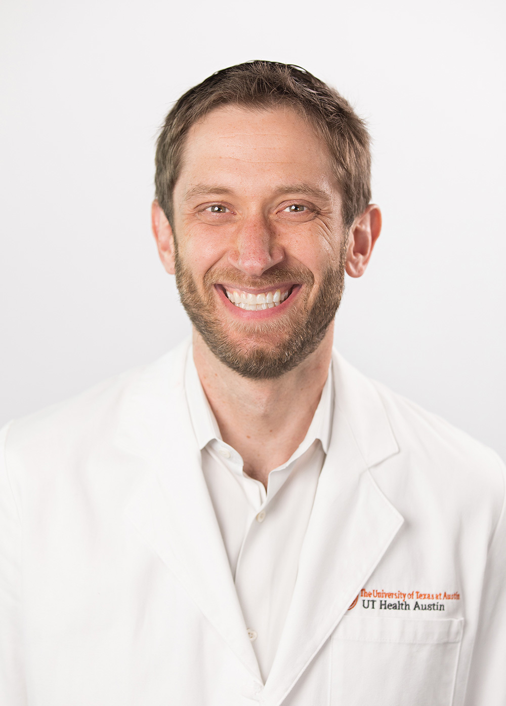 Abdominal transplant surgeon Joel T. Adler, MD, MPH wearing a white coat and smiling in front of a white backdrop.