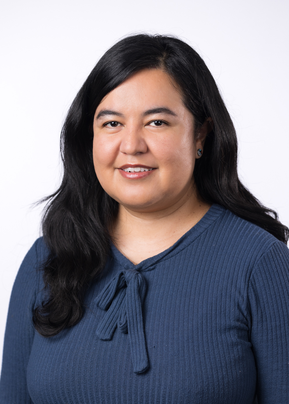 Karen Mendoza smiling in front of a white background. She is wearing a navy blouse.