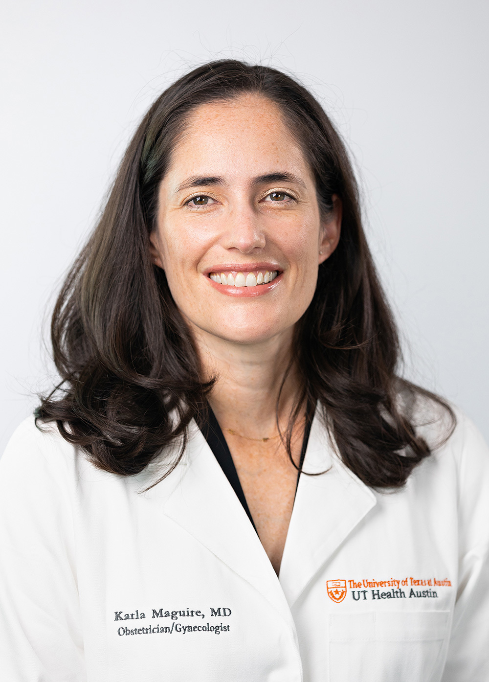 Obstetrician-gynecologist Karla Maguire, MD, MPH, wearing a white coat and smiling in front of a white backdrop.