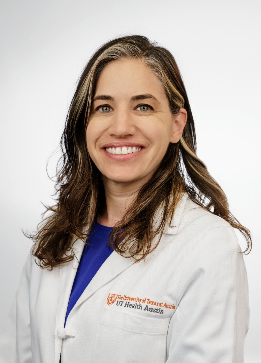 Pediatric psychologist Kathleen Stanton, PhD, smiling in front of a white backdrop. She is wearing a white coat with an embroidered UT Health Austin logo.