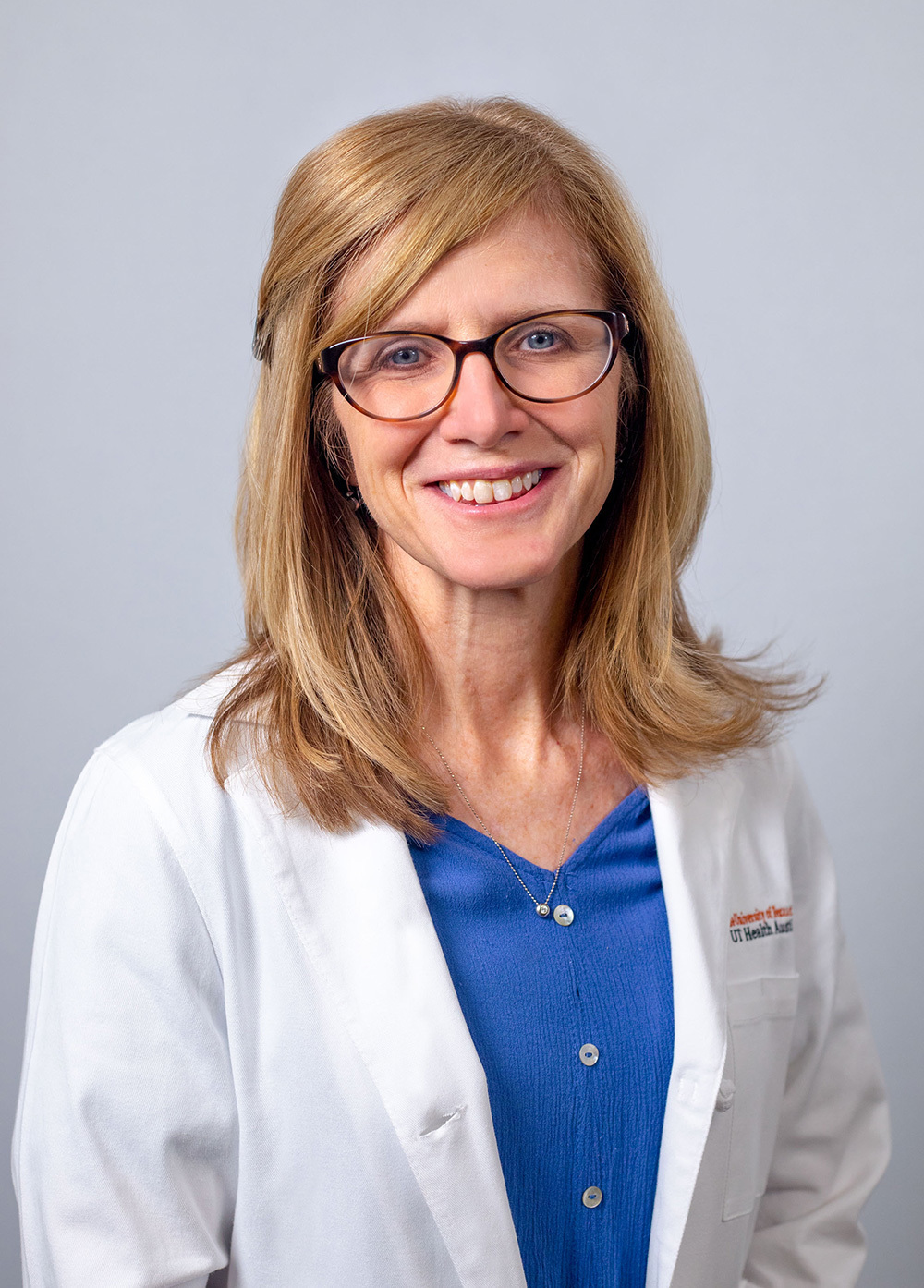 Pediatric nurse practitioner Kelly Gettig APRN, MSN, CBIS, CIC, CPNP-PC/AC, wearing a white coat and smiling in front of a white backdrop.