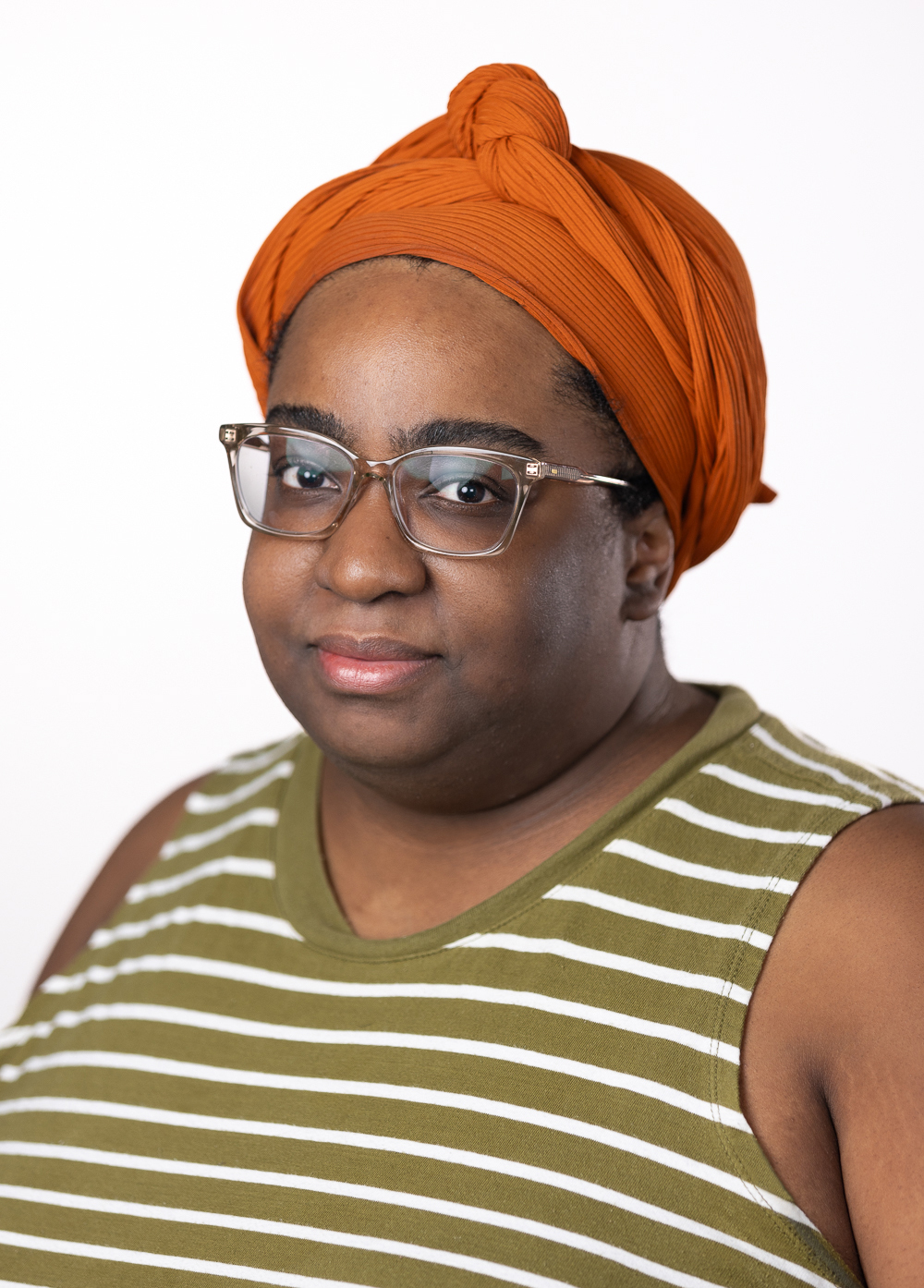 Care navigator Kristina Miller wearing an orange head scarf and striped shirt while smiling in front of a white backdrop.