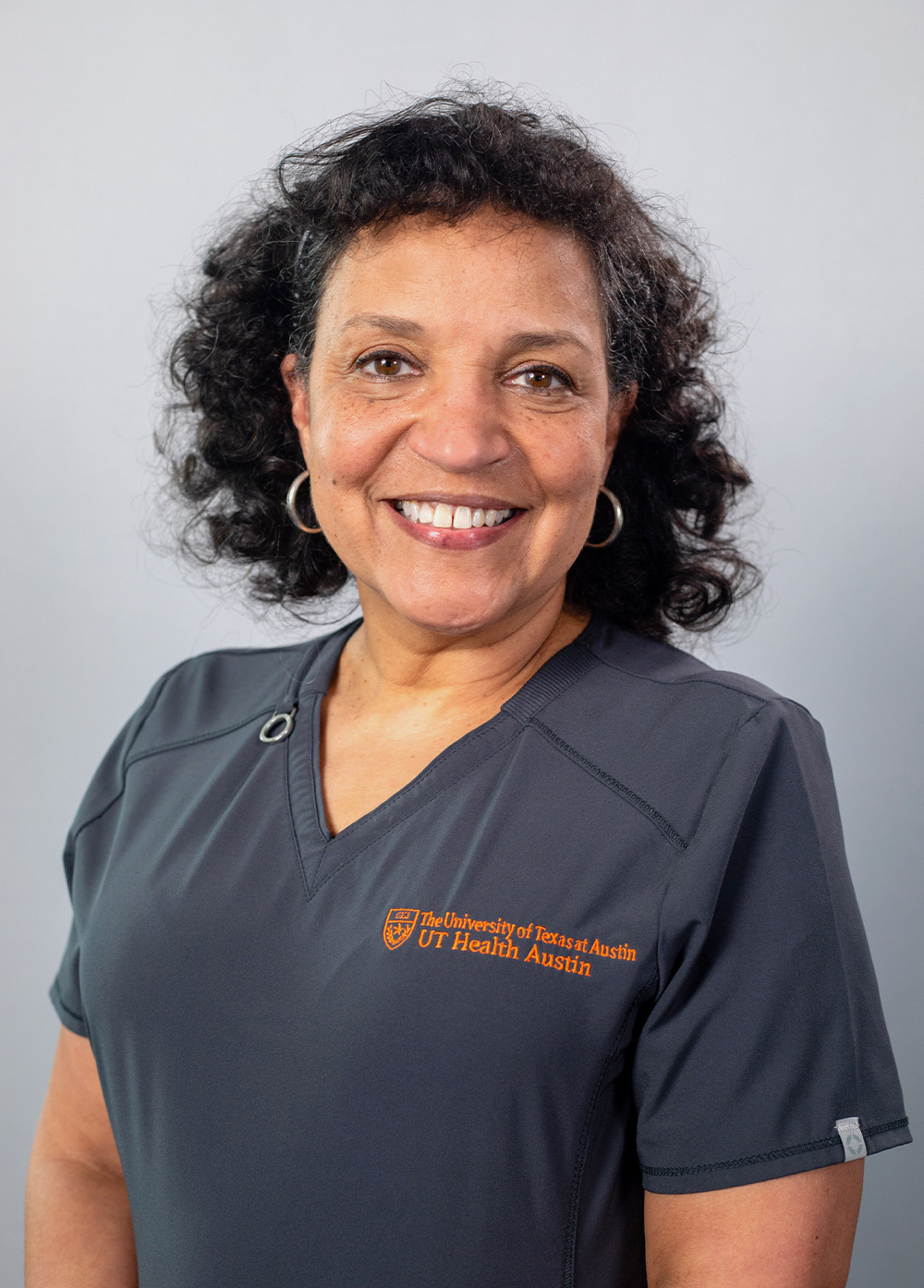 Lori Bolanos wearing dark scrubs and smiling in front of a white backdrop.