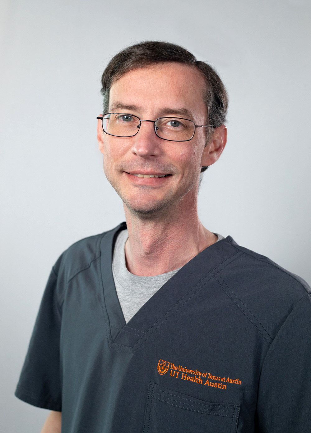 Mark Alder wearing dark scrubs and smiling in front of a white backdrop.