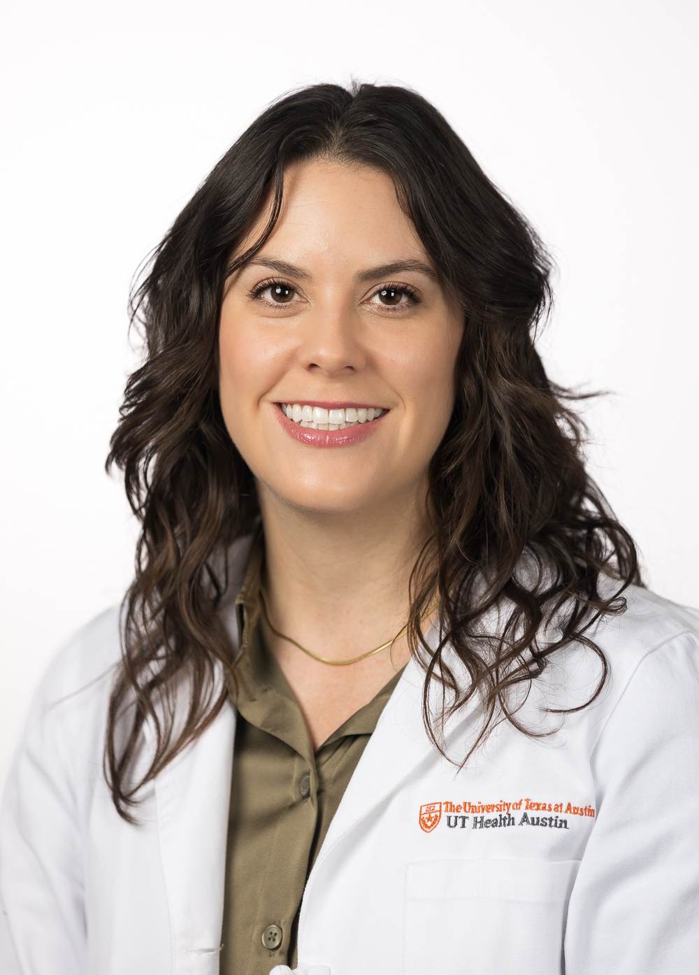 Nurse practitioner Melissa Brown, FNP-C, smiling in front of a white backdrop. She is wearing a white coat with an embroidered UT Health Austin logo.