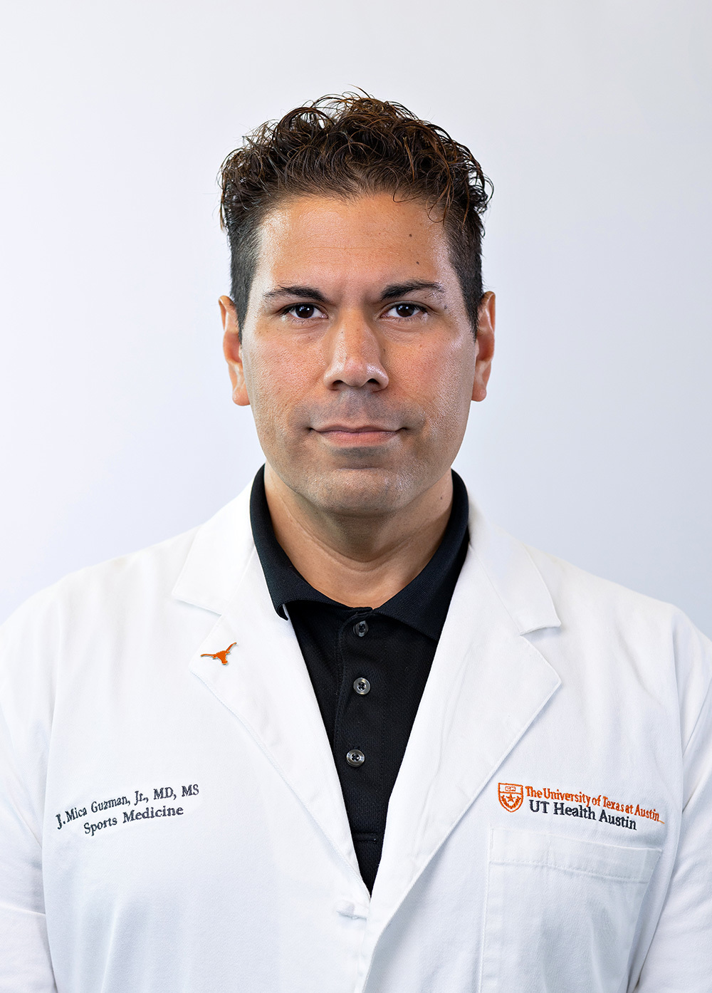 Dr. J. Mica Guzman, Jr., wearing a white coat and smiling in front of a white backdrop.