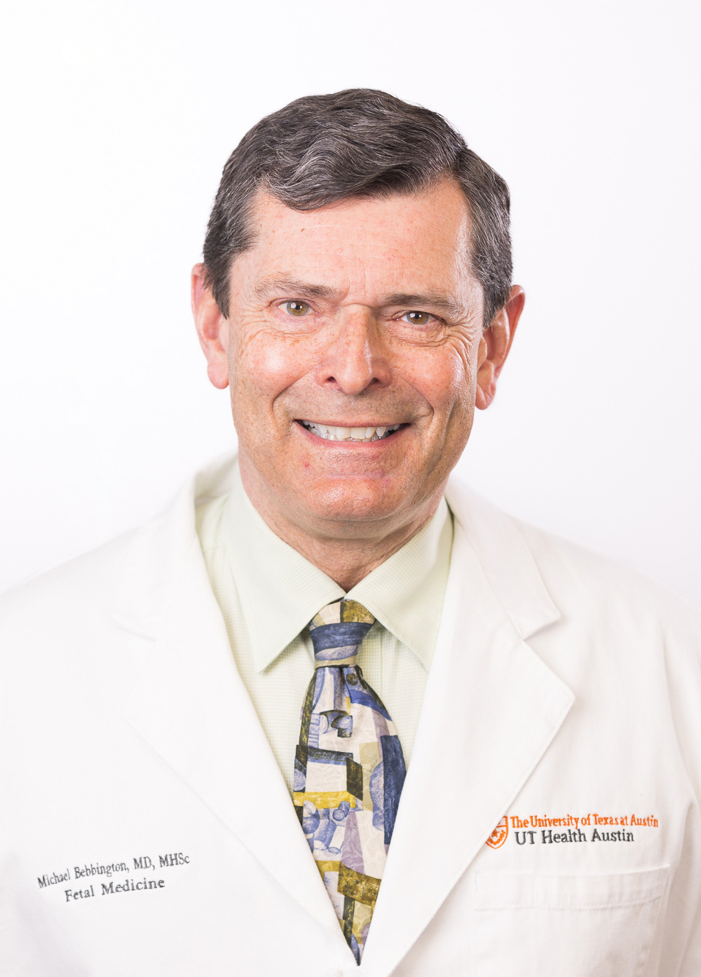 Maternal-fetal medicine specialist Michael Bebbington, MD, MHSc, wearing a white coat and smiling in front of a white backdrop.