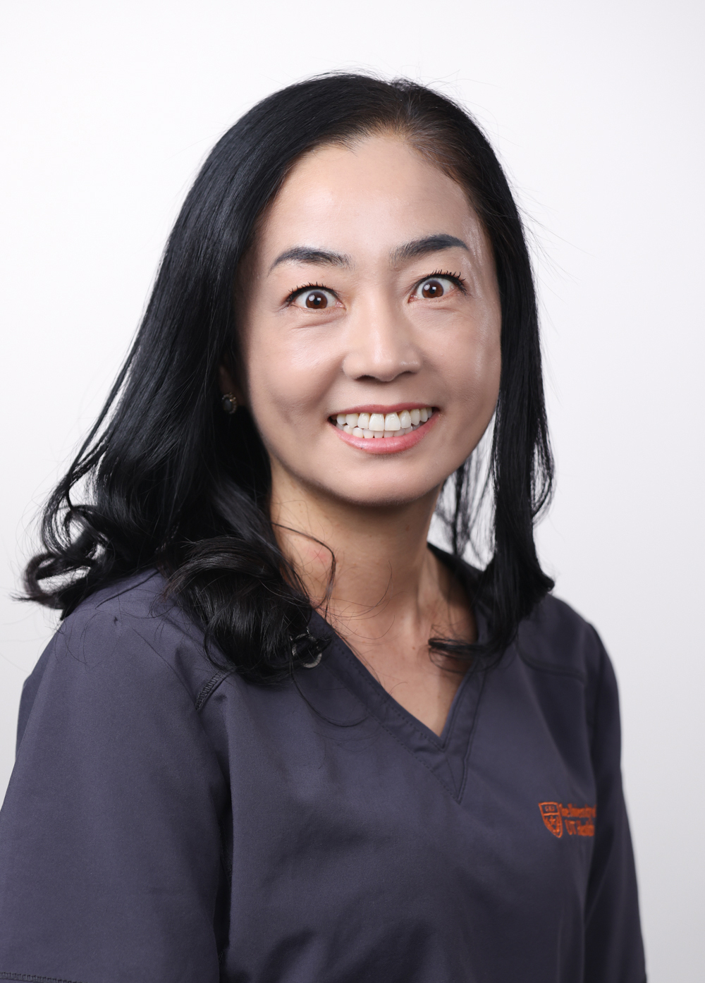 Registered nurse Mihee Yoo, BSN, RN, wearing dark scrubs and smiling in front of a white backdrop.