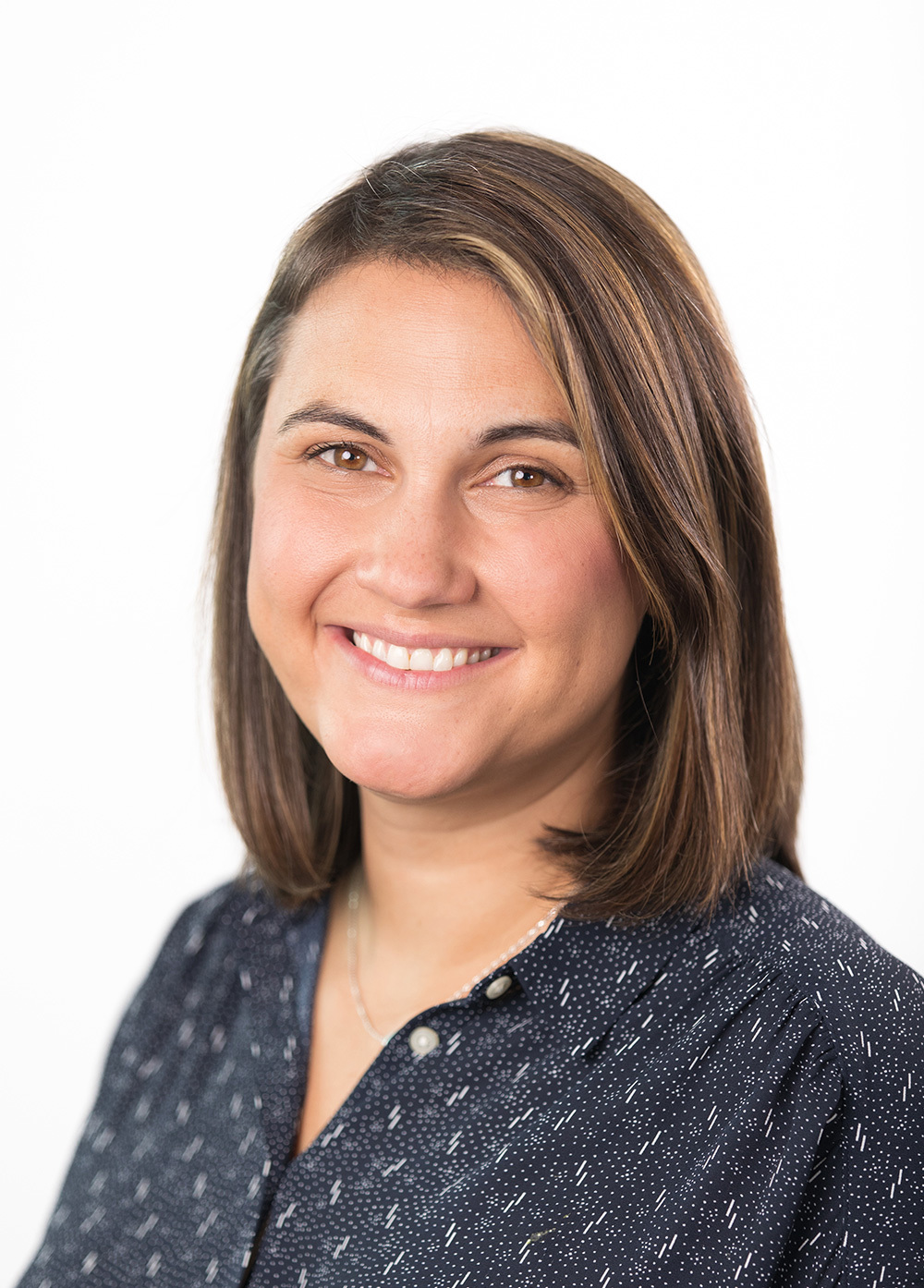 Mikaela Frissell wearing a navy patterned blouse and smiling in front of a white backdrop.