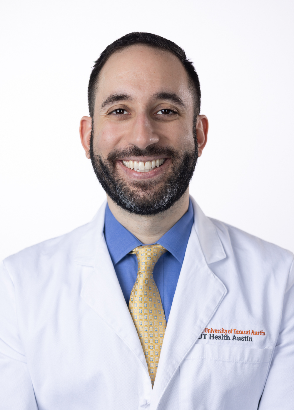 Neurologist Navid Valizadeh, MD, smiling in front of a white backdrop. He is wearing a white coat with an embroidered UT Health Austin logo.