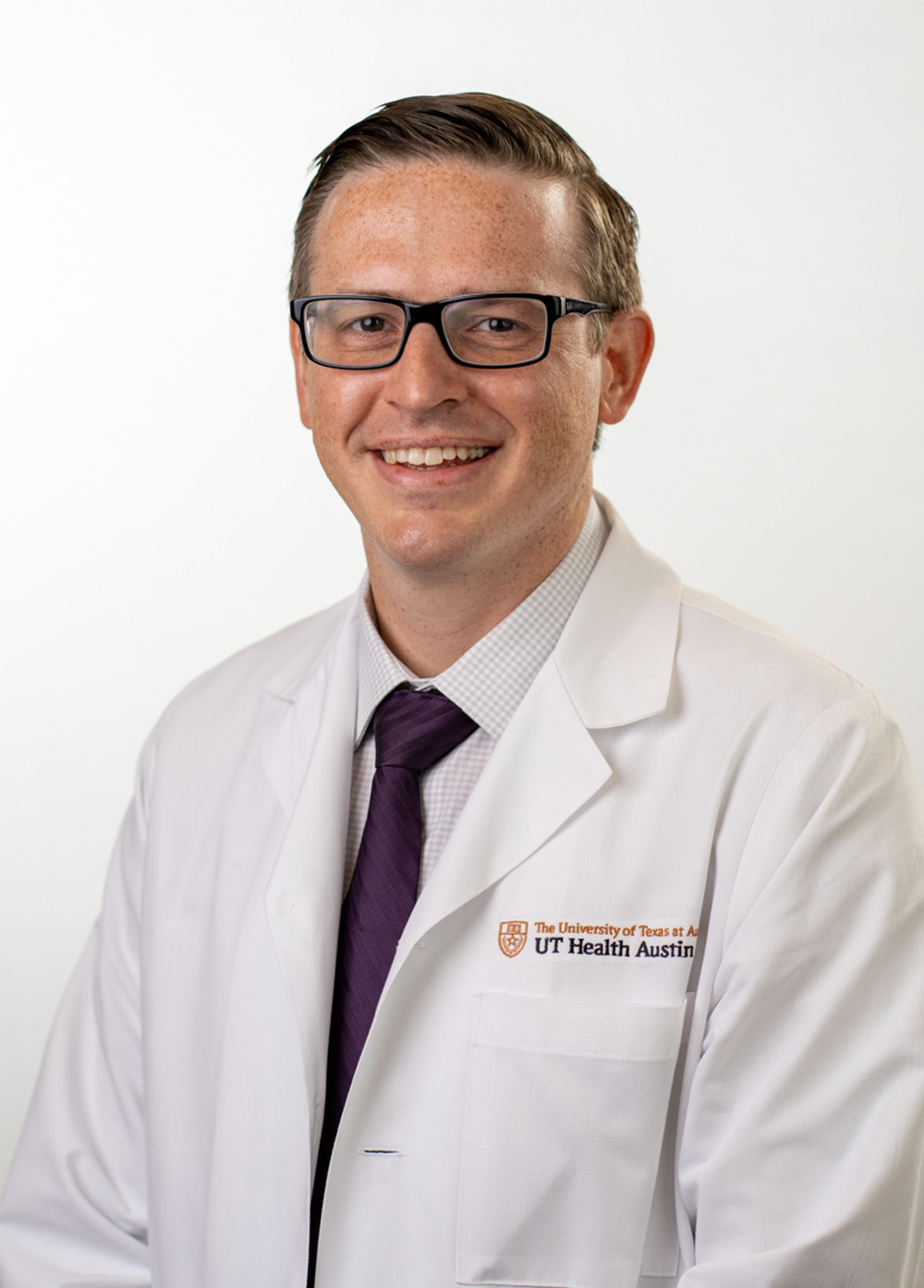 Dr. Neil Venardos wearing a white coat and smiling in front of a white backdrop.