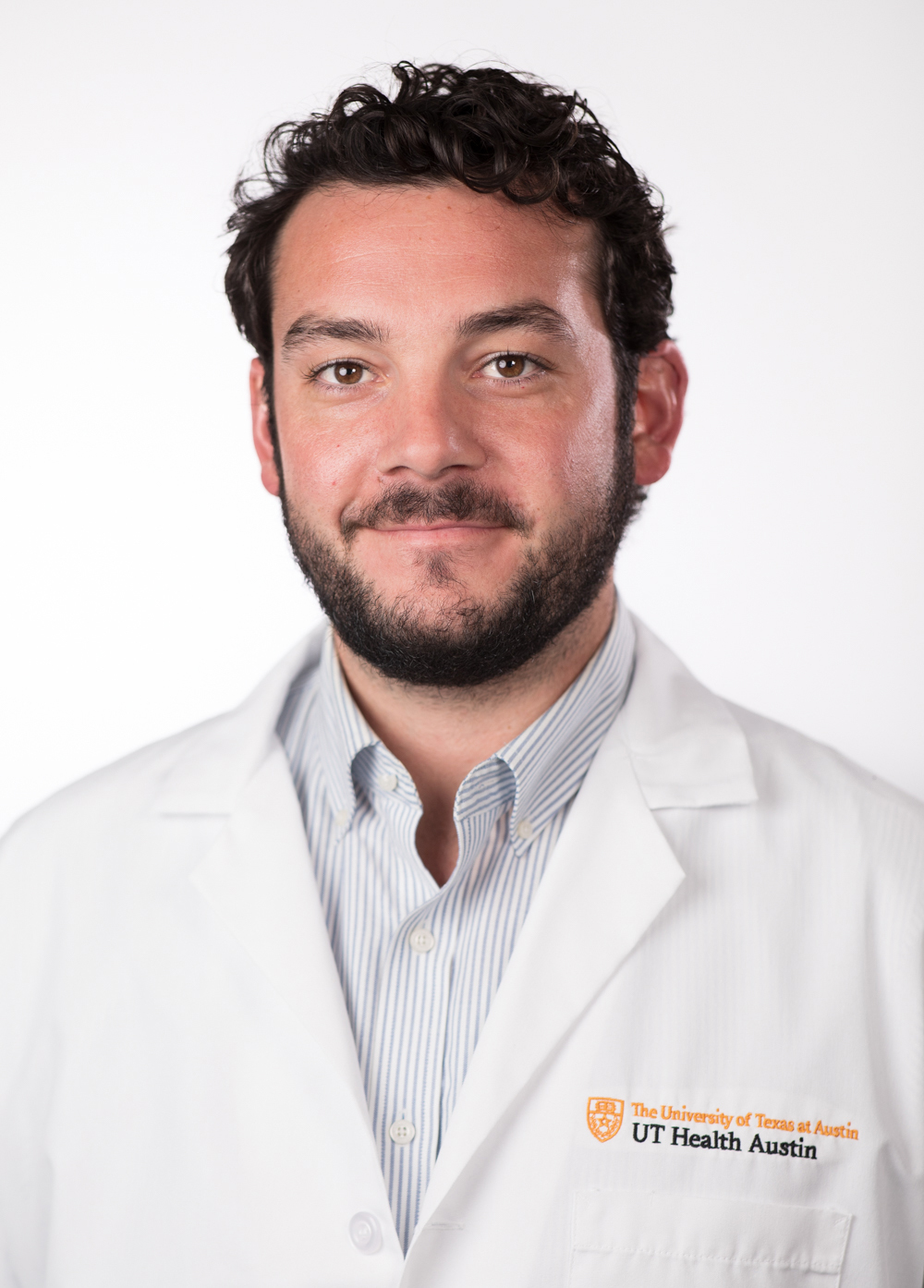 Dr. Nicholas Ortiz wearing a white coat and smiling in front of a white backdrop.