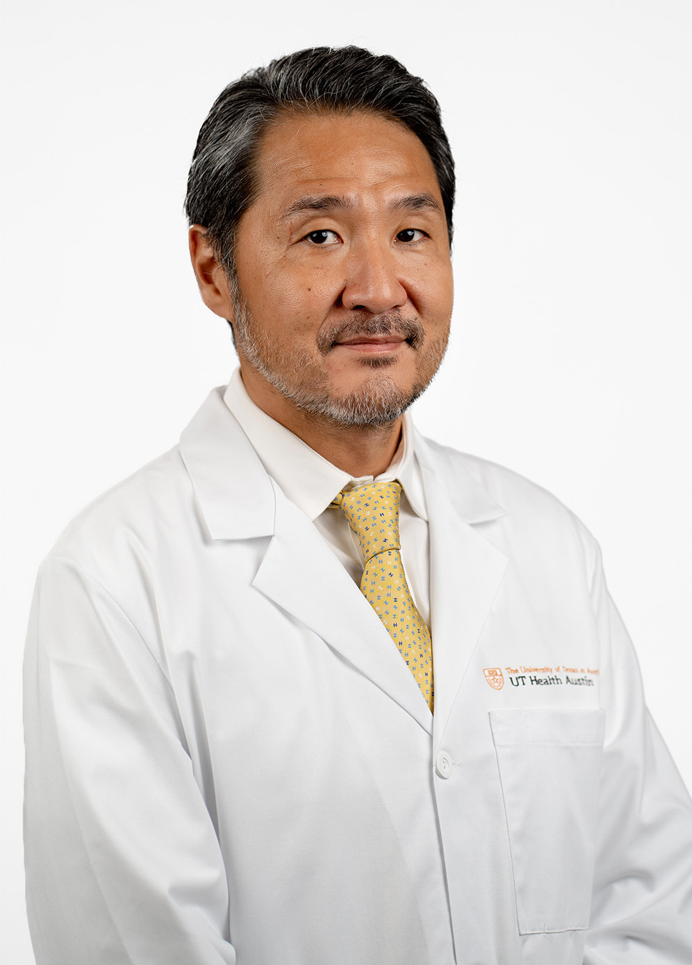 Heart surgeon Ono Masahiro, MD stands in front of a white backdrop with a serious, professional gaze on his face.