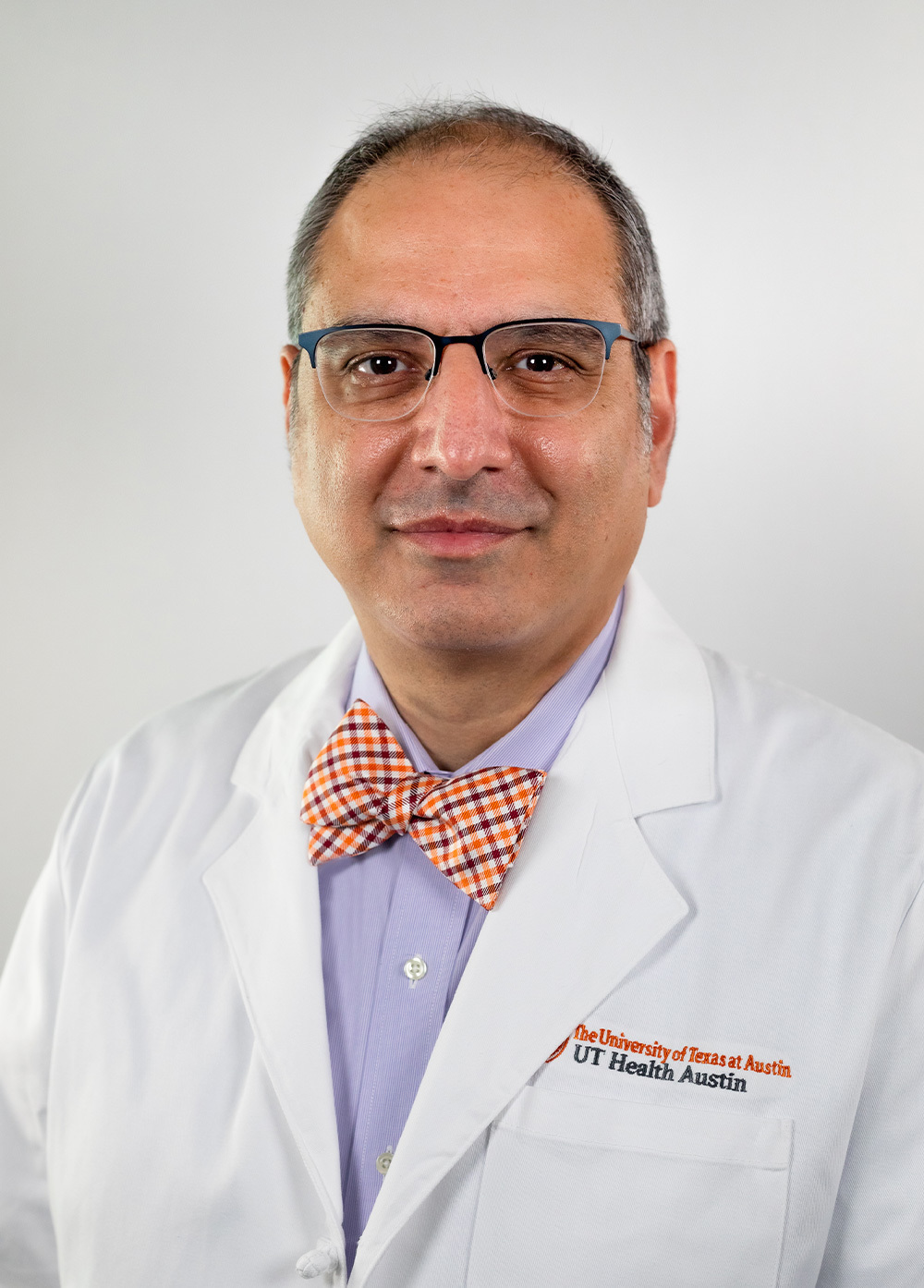Dr. Roozbeh Taeed wearing a white coat and smiling in front of a white backdrop.